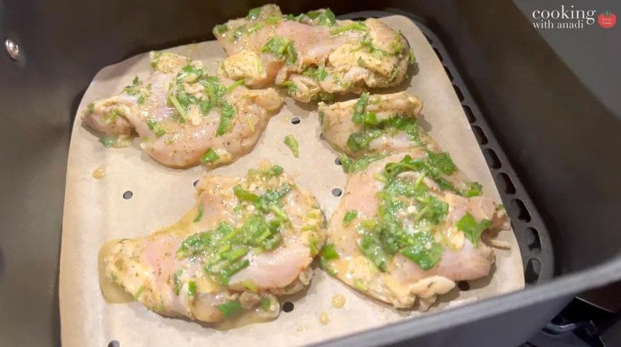 Cuban mojo chicken thighs arranged in air fryer basket, topped with green onions and garlic, ready to cook.
