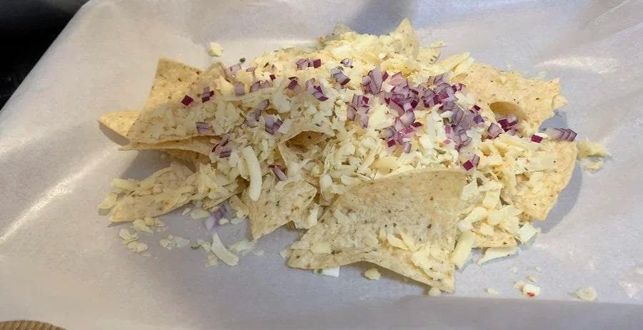 Buffalo chicken nachos topped with shredded cheese, diced white onions, and purple onions on a white plate.