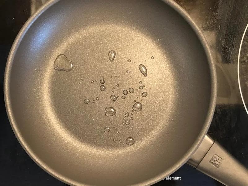 Non-stick pan with melted ghee showing water beads, ready for eggs to be poured in.