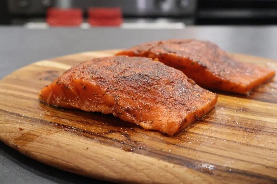 Two seasoned salmon fillets on a wooden cutting board, coated with brown spice rub.