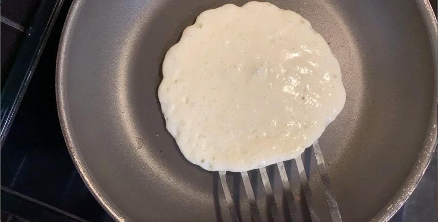 Buttermilk pancake cooking in a skillet with bubbles forming on the surface, ready to flip.