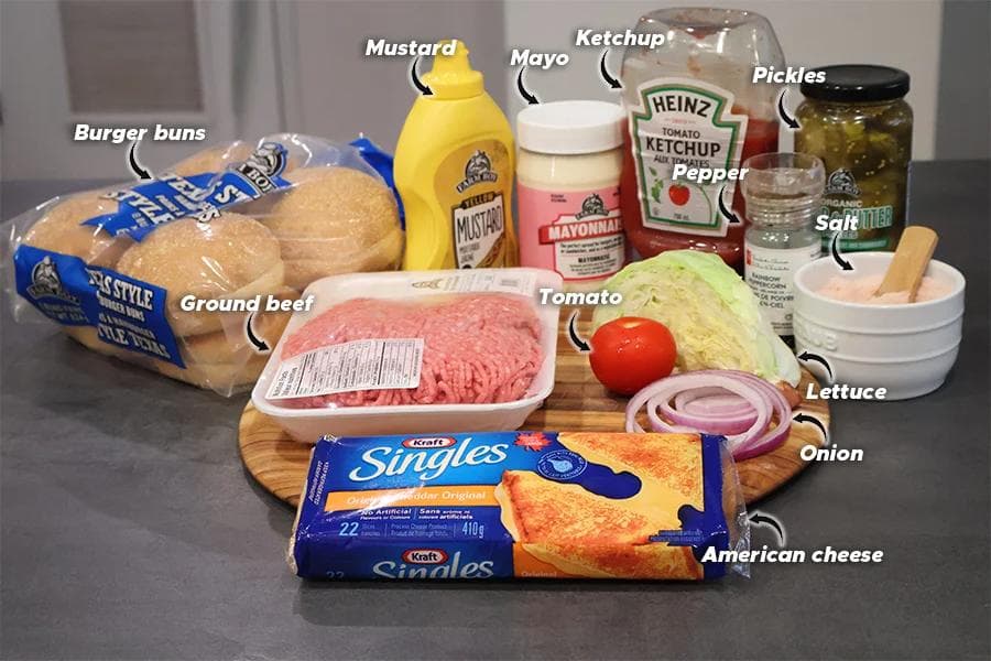 Cheeseburger ingredients laid out including ground beef, buns, sliced cheese, condiments, lettuce, tomato, onions, and seasonings.