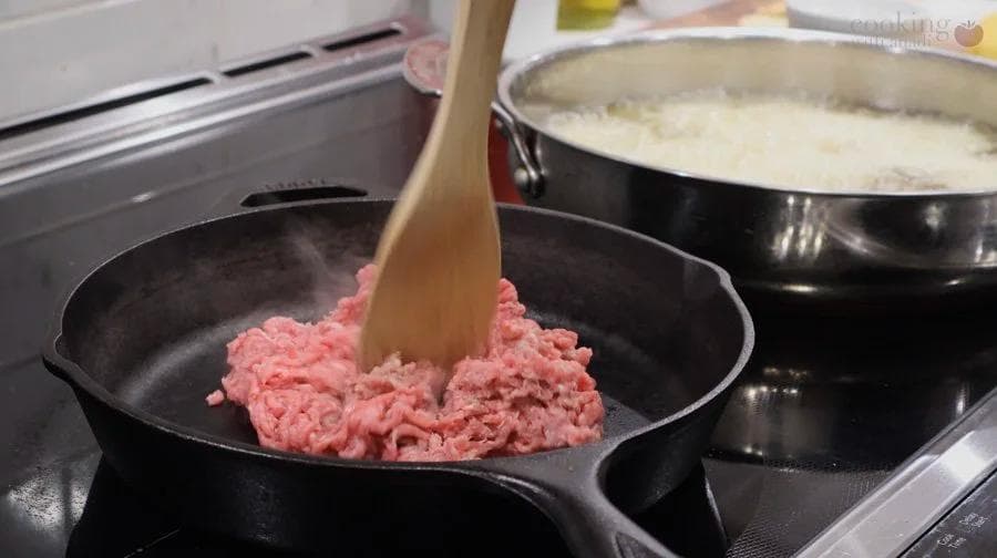 Ground meat mixture being stirred in a skillet during the browning and seasoning step of perkedel daging kentang preparation.