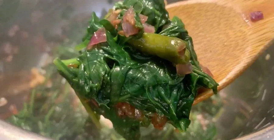 Cooked spinach and paneer being lifted on a wooden spoon from an Instant Pot before blending.