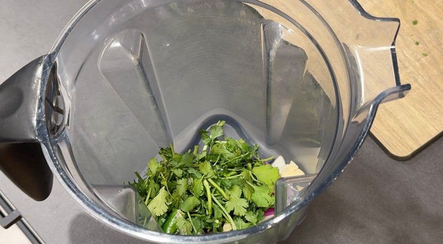 Fresh cilantro and other ingredients in blender bowl, ready to blend for salsa verde.