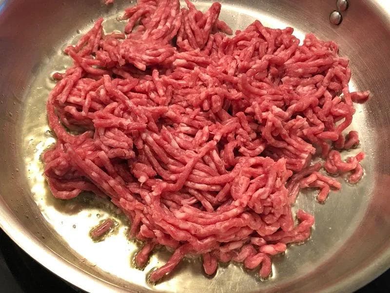 Ground lamb being browned in a stainless steel pan with oil for Shepherd's Pie.