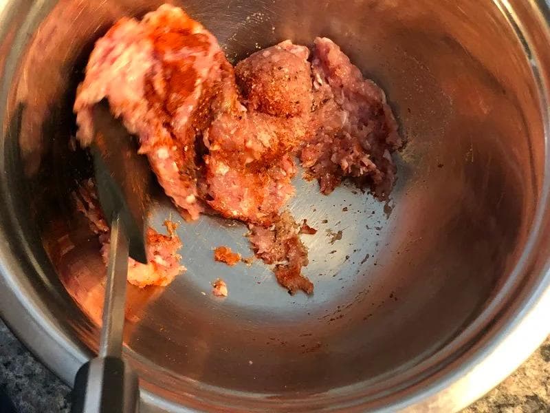 Ground turkey meat mixed with red spices in a metal bowl with a spatula.