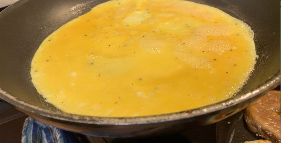 Cooked omelet with melted cheese in the center, seasoned with black pepper, in a dark skillet.