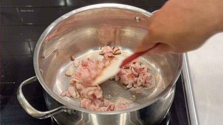 Flour-coated chicken pieces browning in bacon fat in a stainless steel pot.