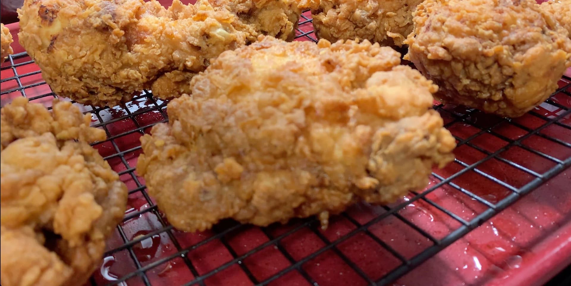 Golden-brown fried chicken pieces cooling on a red wire rack after frying.
