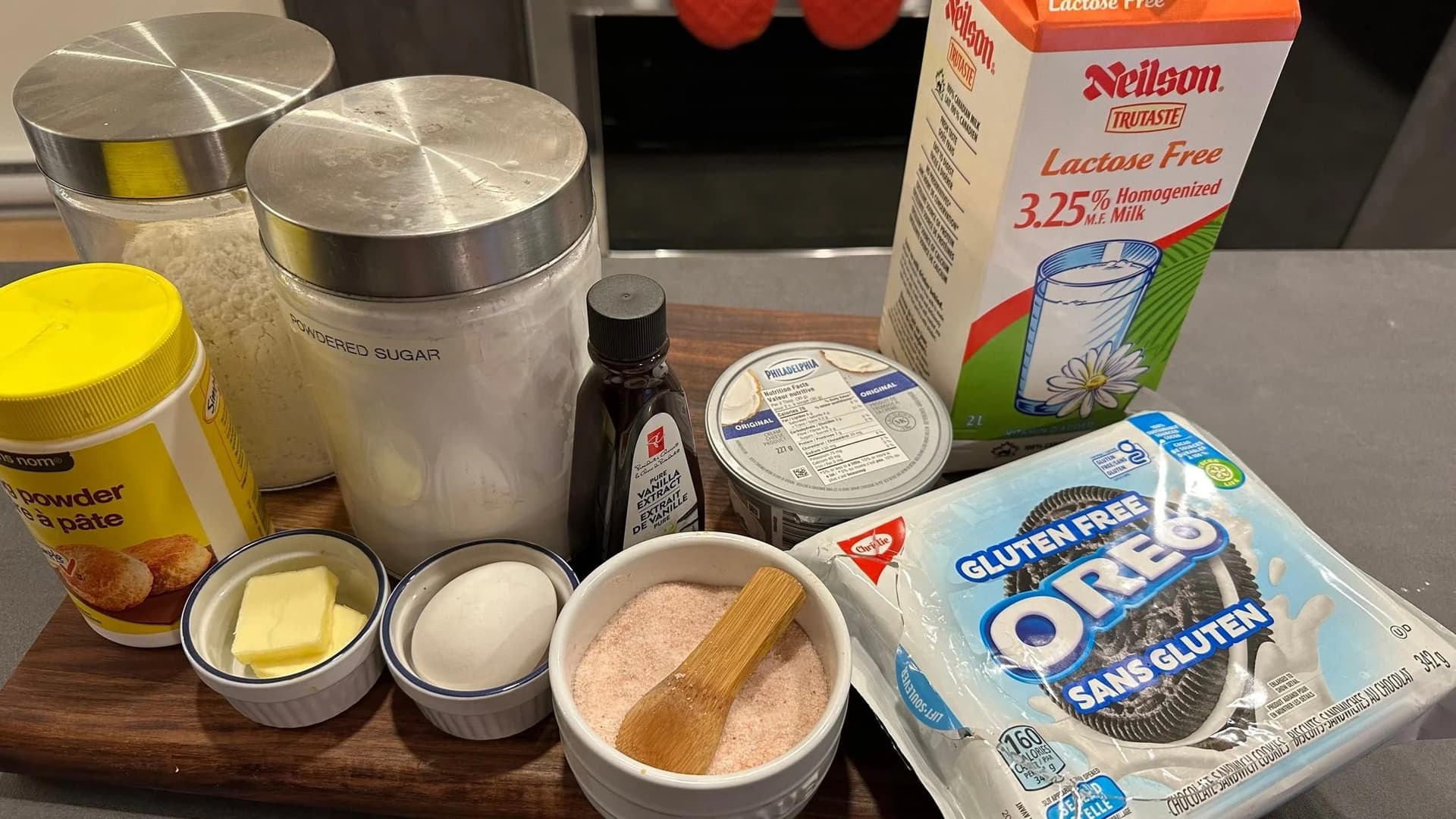 Ingredients for gluten-free Oreo cheesecake pancakes displayed on a wooden surface, including butter, eggs, milk, sugar, Oreos, and peanut butter.