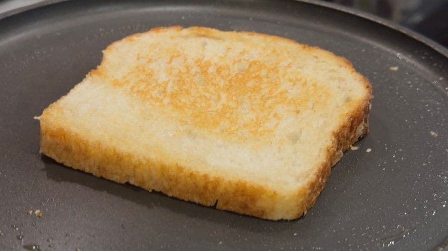 Golden-brown toasted bread slice on a skillet, ready for tuna salad assembly.
