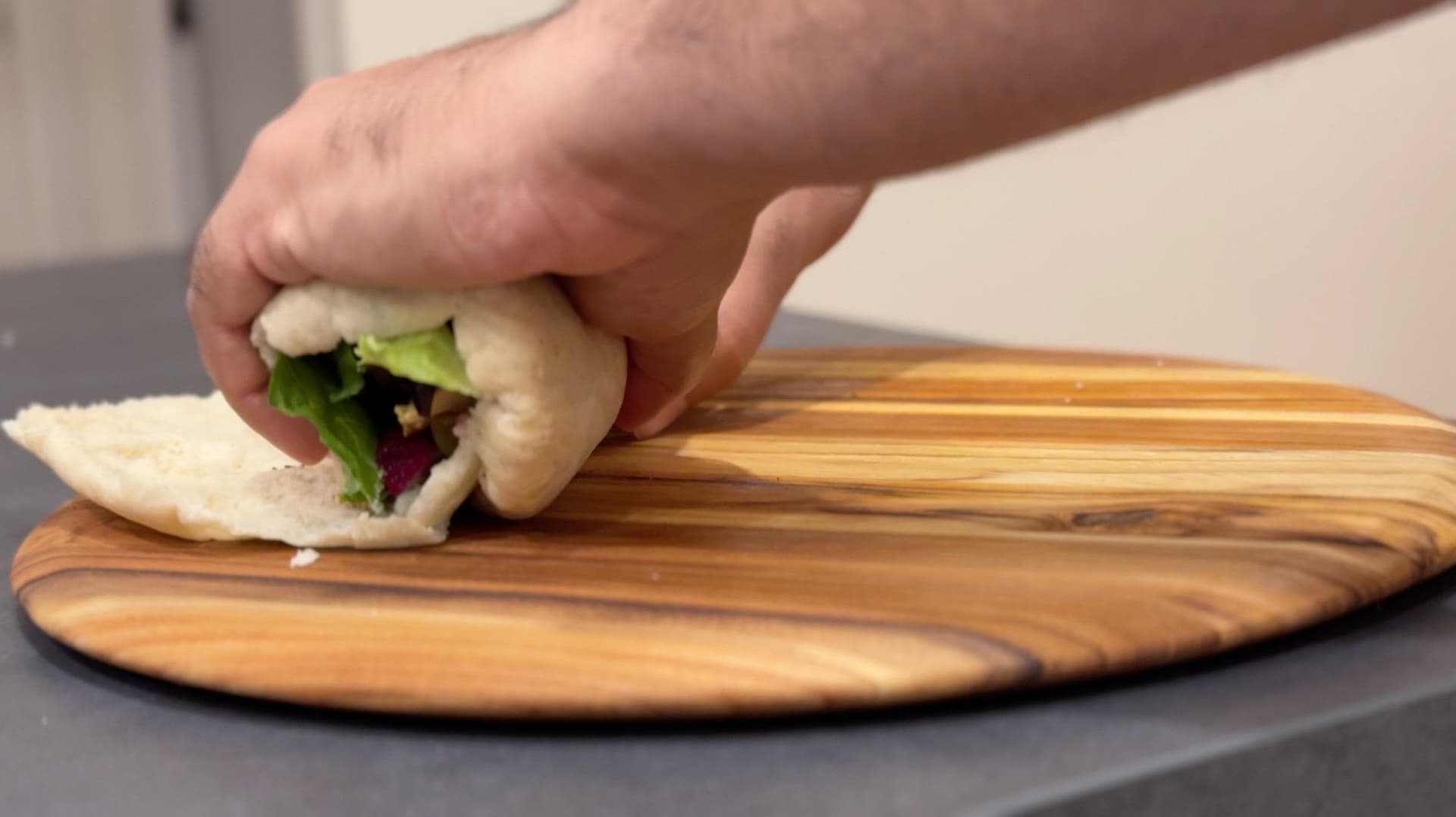 Hand holding a wrapped chicken shawarma with lettuce and vegetables visible inside a pita on a wooden board.