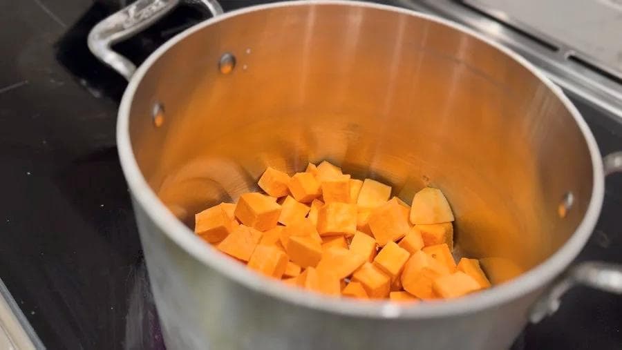 Diced sweet potatoes in a white pot, ready to be cooked in milk for mashed potatoes.
