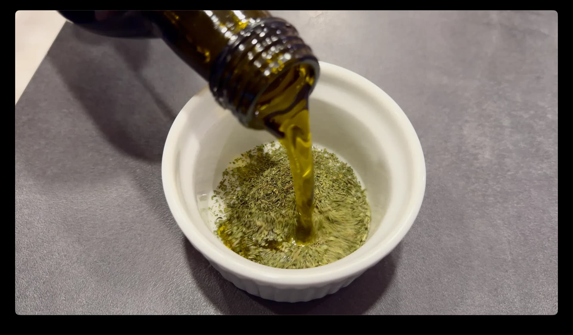 Olive oil being poured into a white bowl containing lemon and herb seasoning paste.