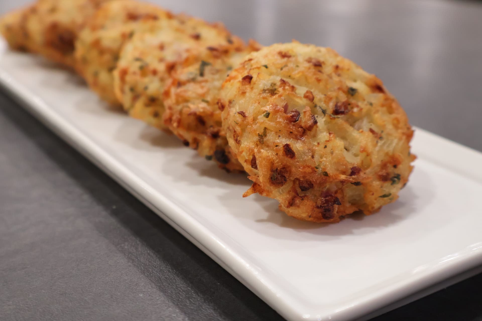 Golden-brown Venezuelan rice fritters with cheese arranged on a white rectangular plate against a gray surface.