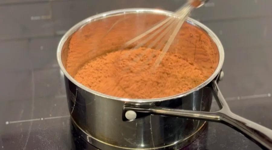 Cocoa powder and sugar mixture being whisked in a saucepan on the stovetop.