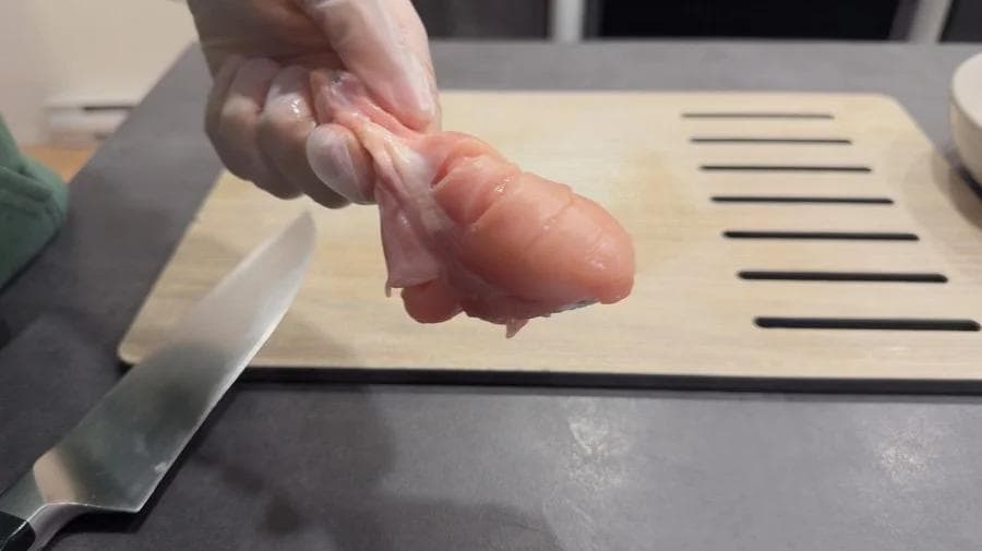 Hand demonstrating deep gashes cut into raw chicken drumstick for tandoori marinade preparation.