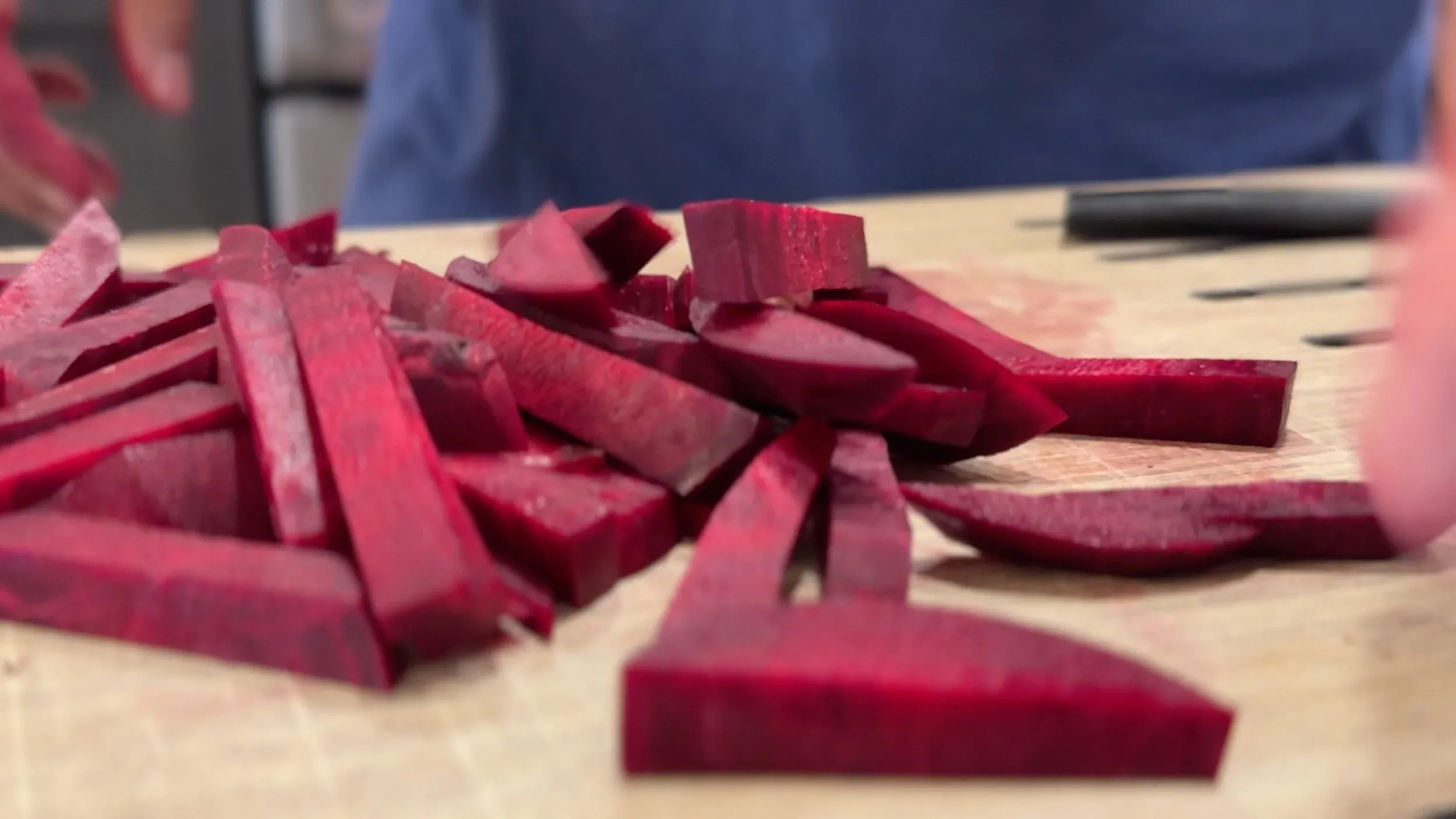 Sliced beets cut into 1/2 inch strips arranged on a wooden cutting board.