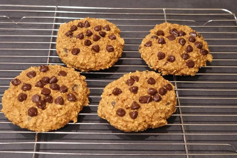Four baked pumpkin chocolate chip cookies cooling on a wire rack.