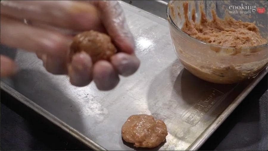 Hands shaping ground chicken mixture into a nugget on a floured baking tray, with a bowl of mixture visible in the background.