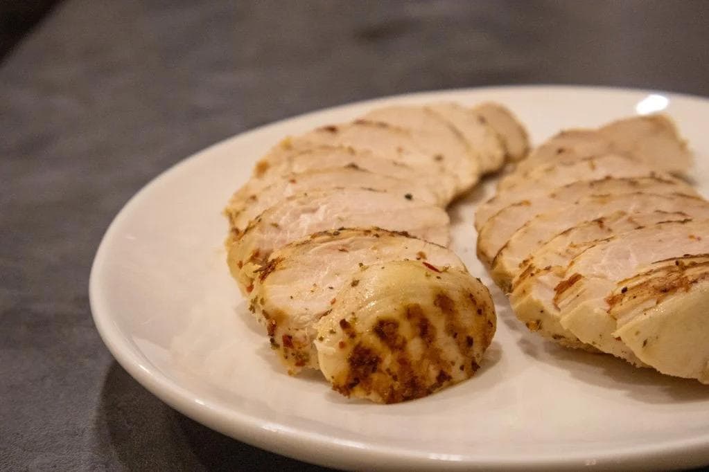 Sliced Italian herb grilled chicken breast on a white plate, showing grill marks and seasoning.