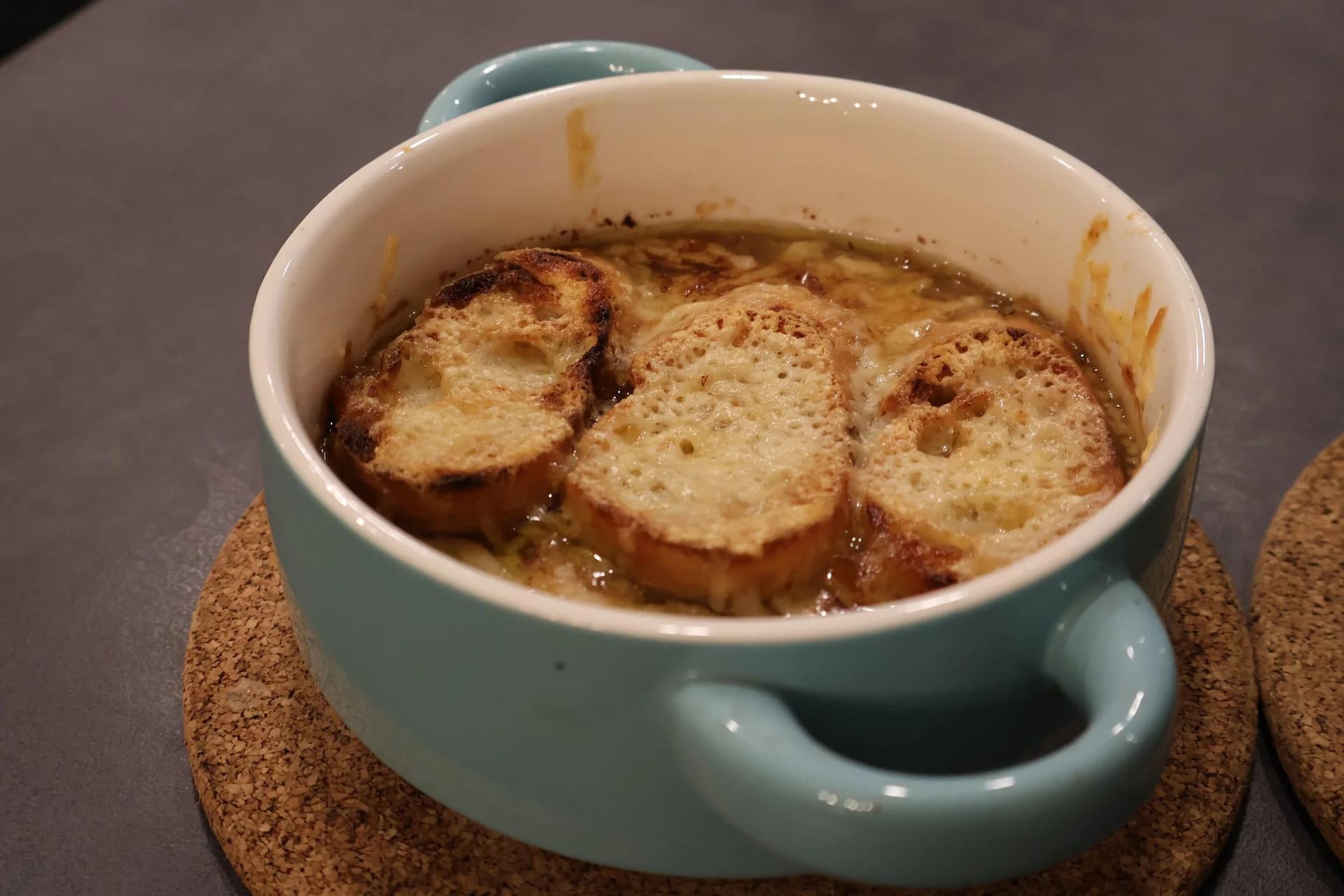 French onion soup in a light blue bowl topped with melted cheese and toasted bread slices.
