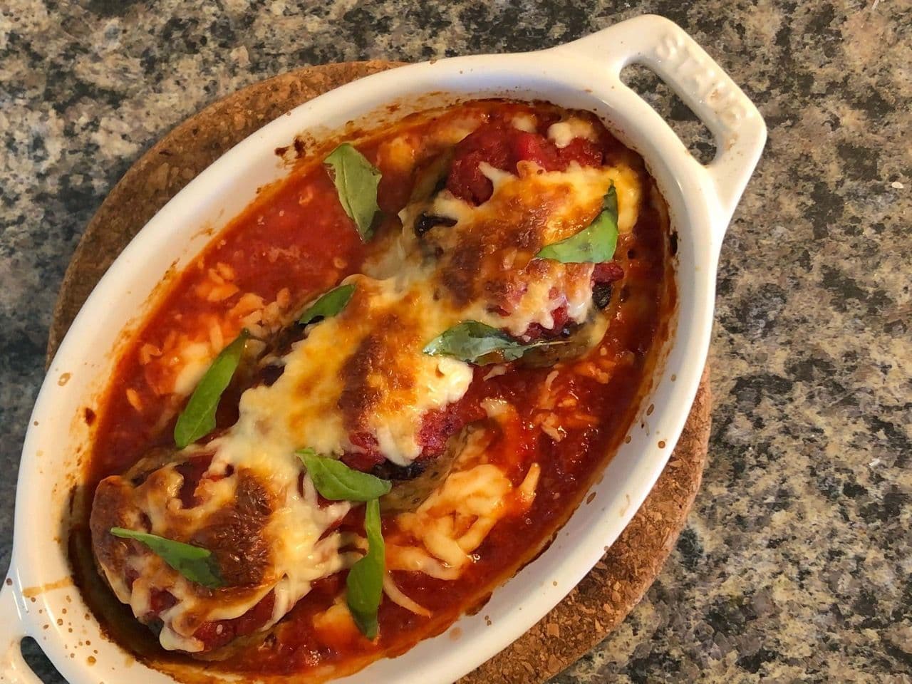 Cheesy oven-baked meatball casserole in marinara sauce with melted cheese and fresh basil garnish in a white baking dish.