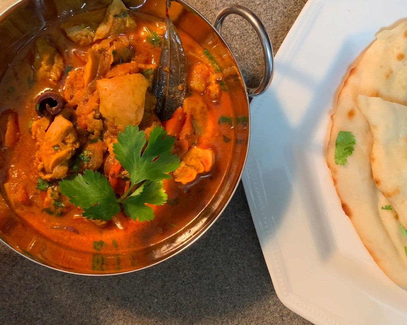 Homestyle chicken curry in a copper pot with fresh cilantro, served with naan bread on a white plate.