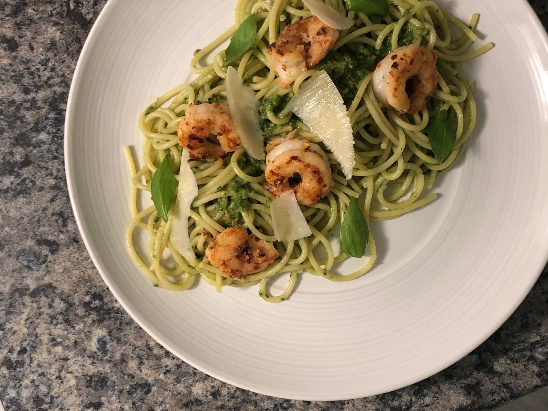 Creamy spinach pesto zucchini noodles topped with pan-seared shrimp, fresh basil, and shaved parmesan on white plate.