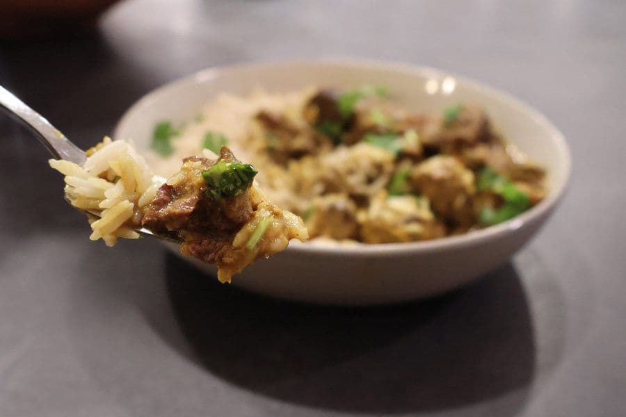 Spoonful of Balinese beef rendang with rice held over a bowl garnished with cilantro.