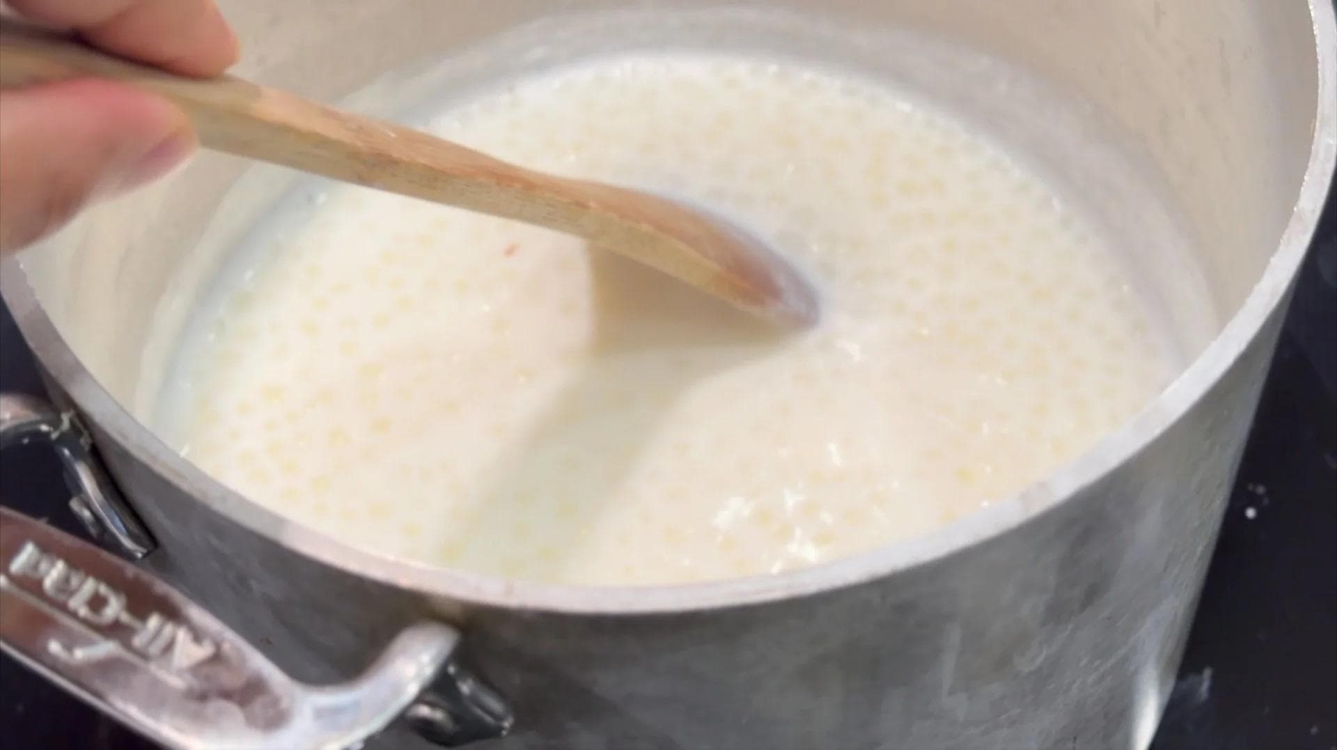 Creamy sabudana kheer being stirred in a pot with a wooden spoon during cooking.