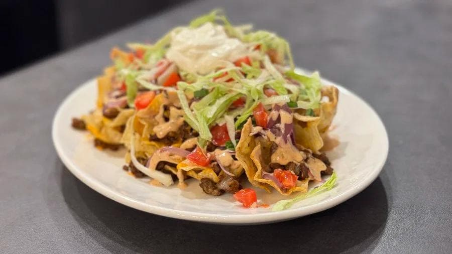 Crispy cheeseburger nachos topped with shredded cheese, red peppers, and green onions on a white plate.