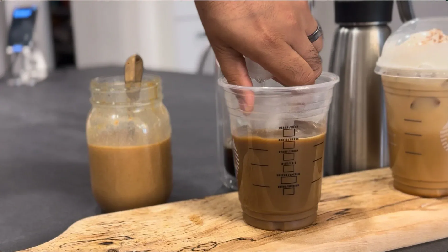 Hand stirring pumpkin spice and coffee together in a clear measuring cup on a wooden surface.