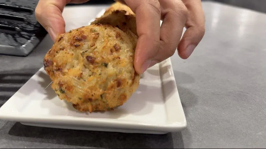 Golden-brown Venezuelan rice fritter with cheese being held above a white plate, showing crispy exterior texture.