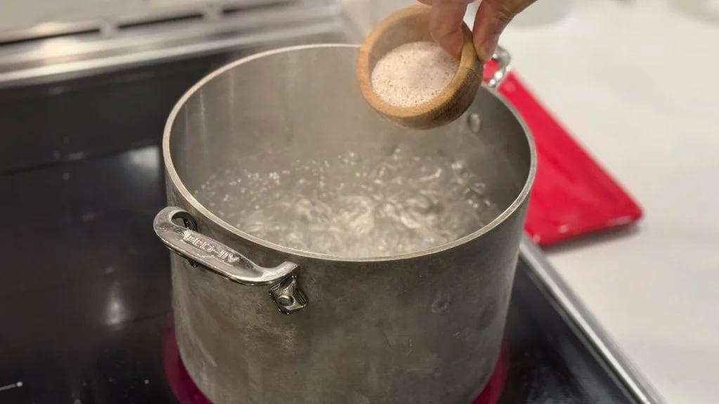Salt being added to boiling water in a pot for parboiling potatoes.