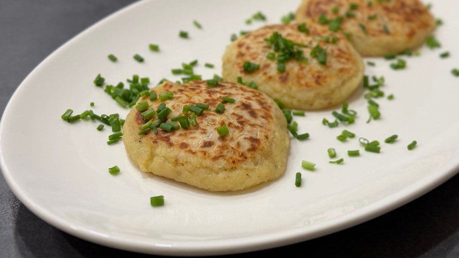 Three golden-brown cheese-stuffed potato pancakes garnished with fresh chopped chives on a white plate.