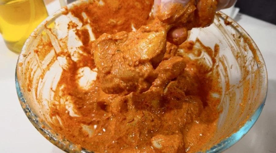 Tandoori chicken marinade in a glass bowl with spiced yogurt coating and chicken pieces ready for air frying.