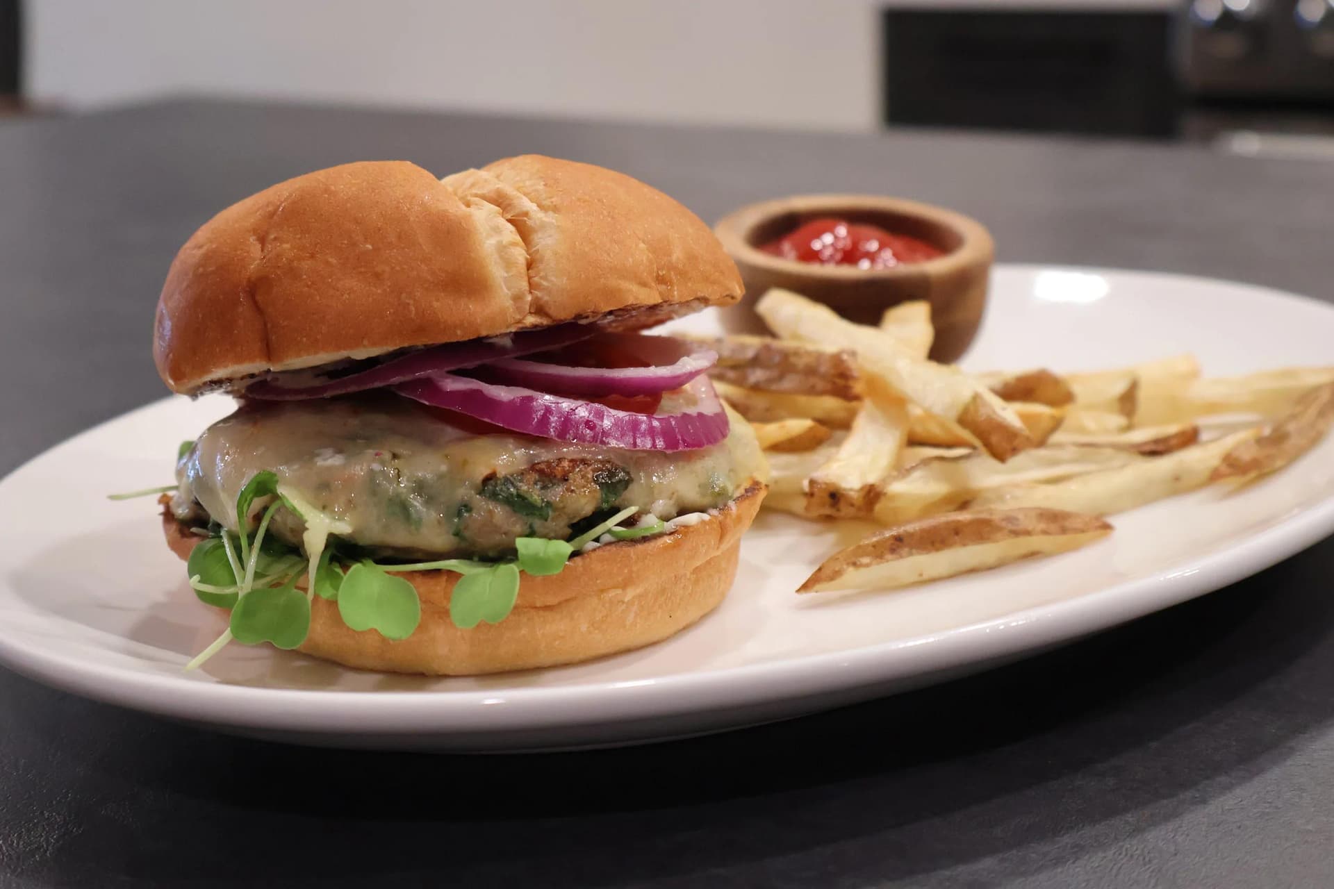 Spinach turkey burger on toasted bun with melted cheese, red onion, and microgreens, served with french fries and ketchup.