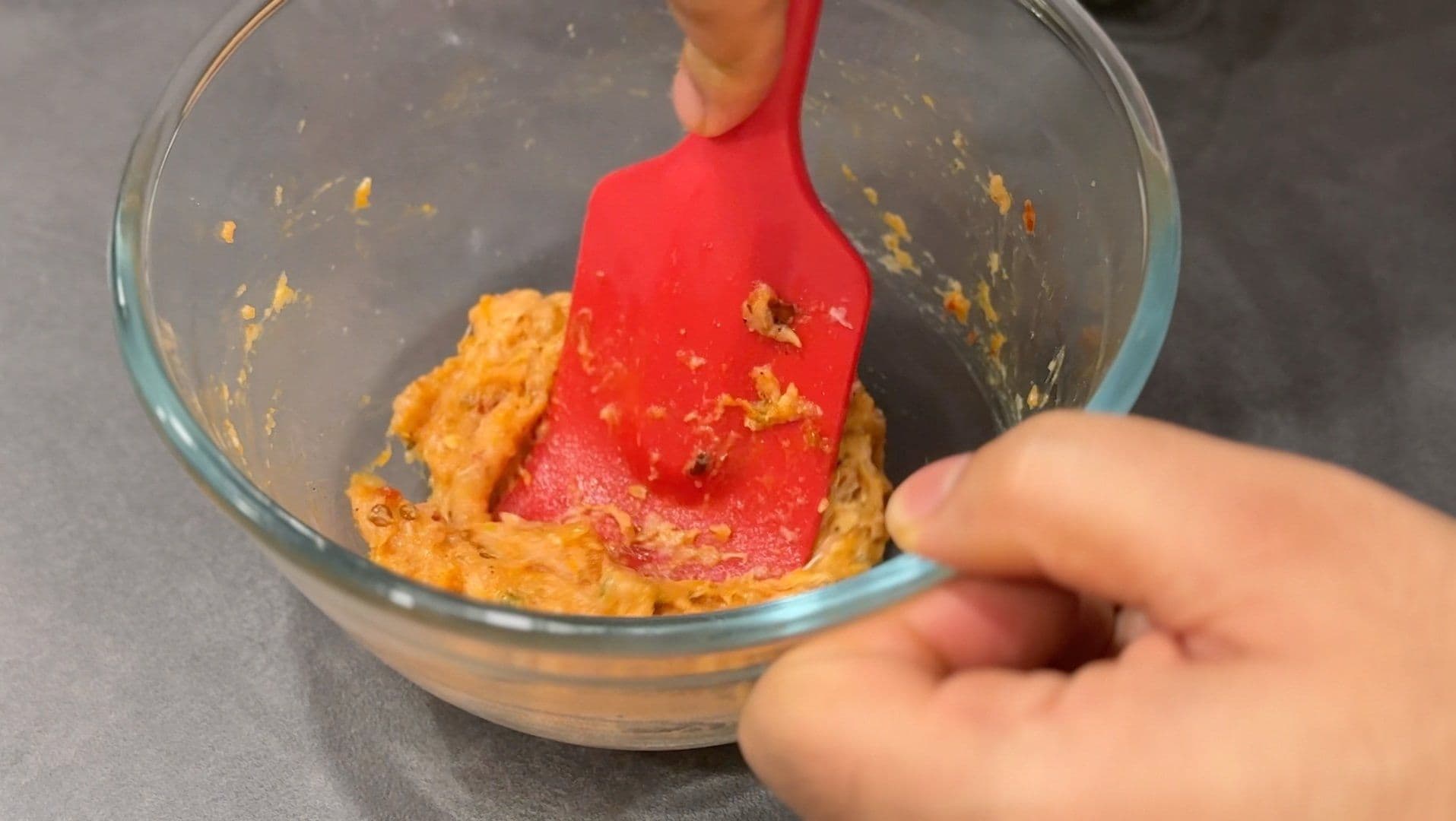 Hand mixing orange ground meat mixture with red spatula in glass bowl