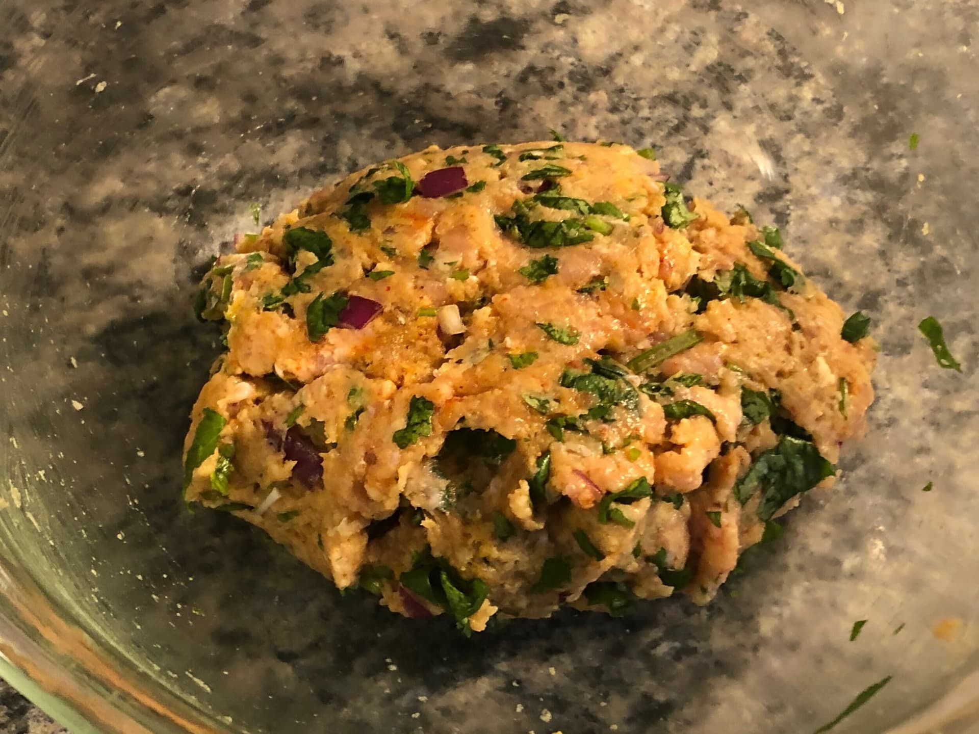Chicken seekh kebab mixture combined in glass bowl with herbs and spices visible throughout