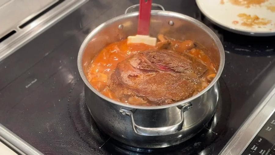 Pot roast braising in a Dutch oven with browned meat partially submerged in rich brown broth on the stovetop.