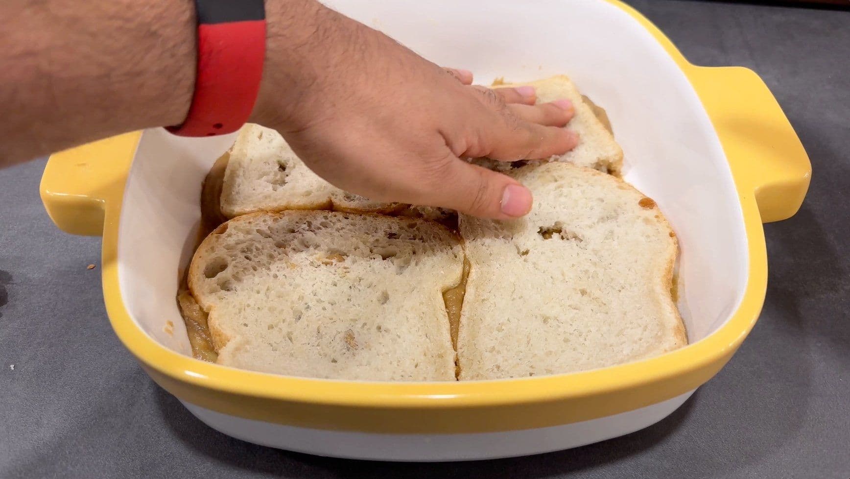 Hand arranging bread pieces in yellow casserole dish with egg mixture for overnight French toast casserole.