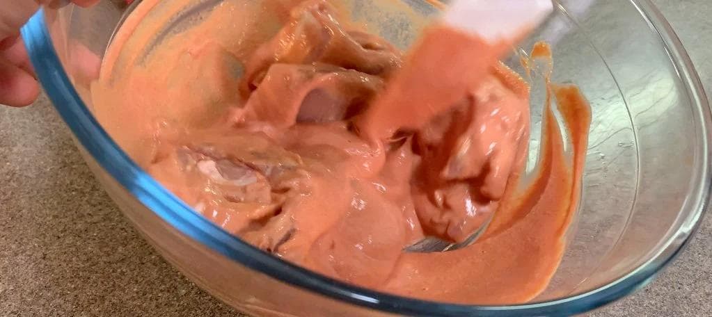 Marinated chicken mixed with yogurt and tomato paste in a glass bowl, showing the combined ingredients before cooking.
