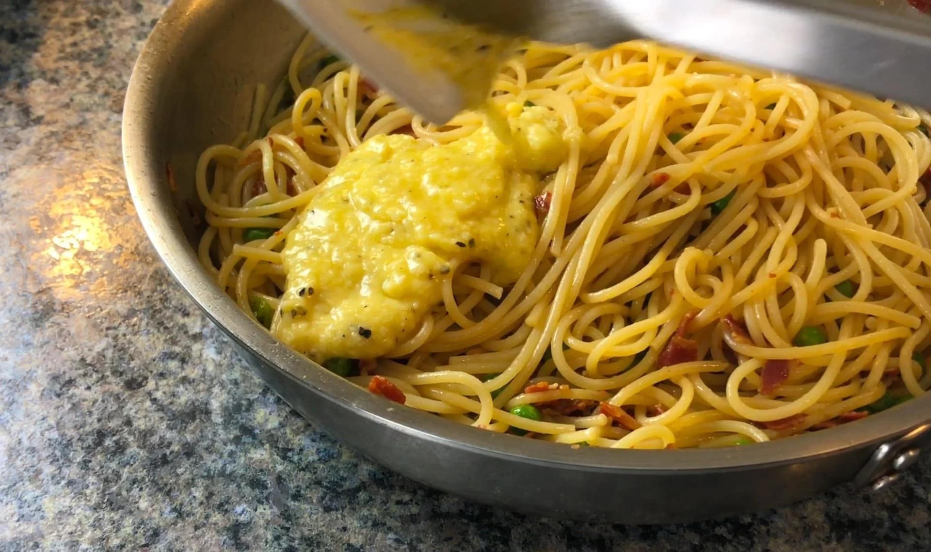 Spaghetti carbonara being stirred in a pan with creamy egg and cheese sauce coating the noodles.