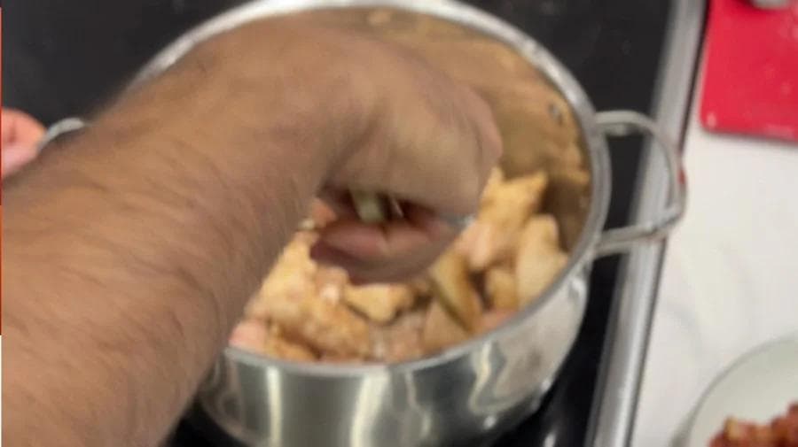 Hand holding slotted spoon removing browned chicken pieces from pot with bacon fat.