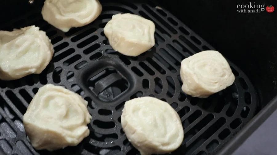 Mashed potato pinwheels arranged in an air fryer basket during cooking.