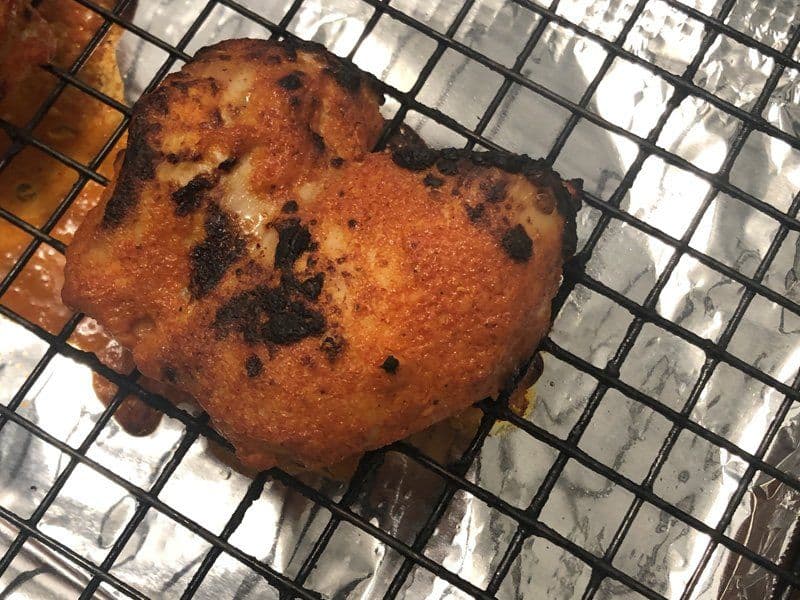 Tandoori chicken tikka piece on wire rack, golden-brown with charred spices, ready for serving.