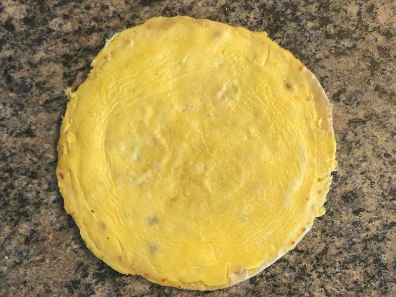 Cooked yellow paratha rolled flat on a granite countertop, ready for filling.
