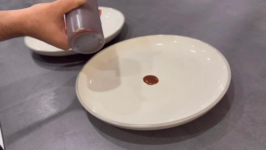 Squeezing caramel sauce onto a white plate with a baked puff pastry apple pie centered on top.